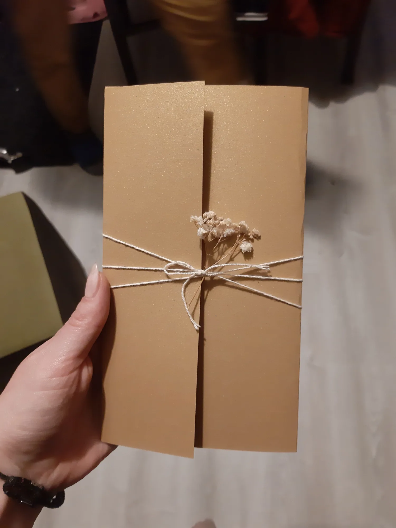 A wedding invitation card from a gold cardboard paper, twine bow and gypsophila.