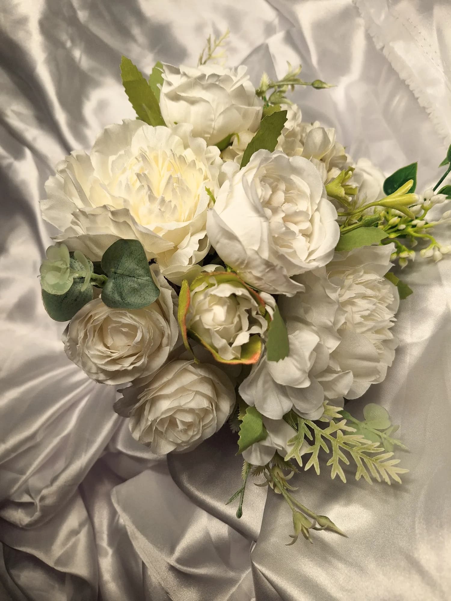 A bridal bouquet of white roses, peonies and green foliage.